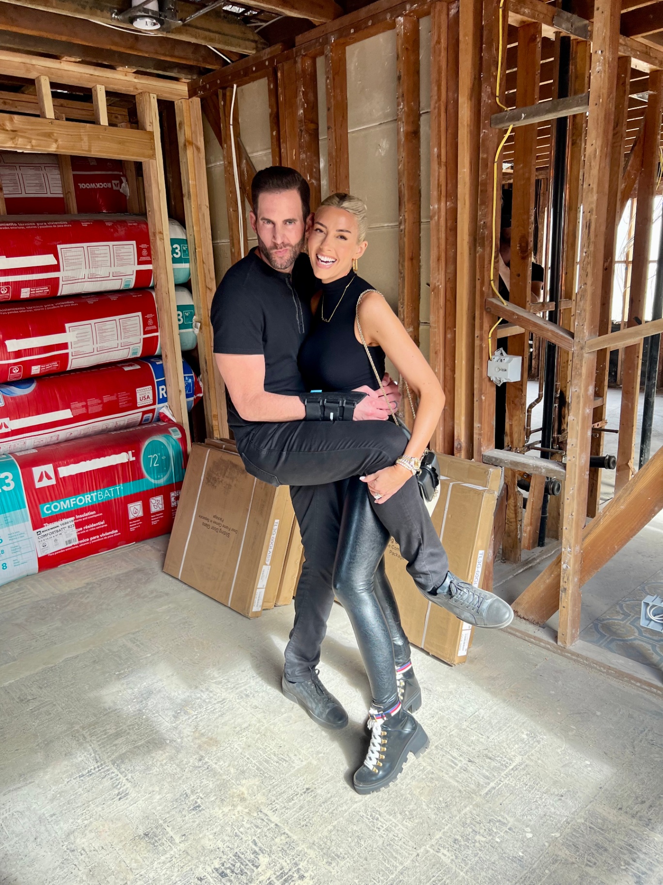 Couple posing inside a home under renovation, framed by exposed studs and insulation