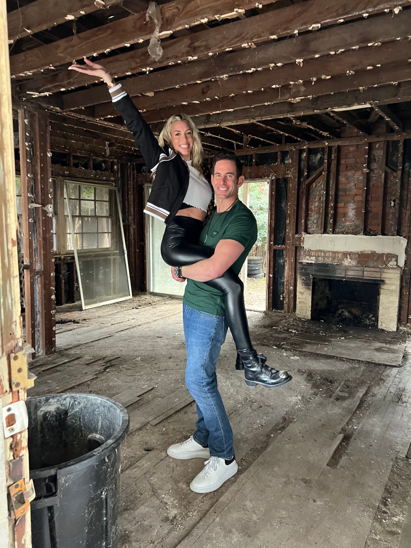 Couple posing inside a stripped-down house interior with exposed framing and brick