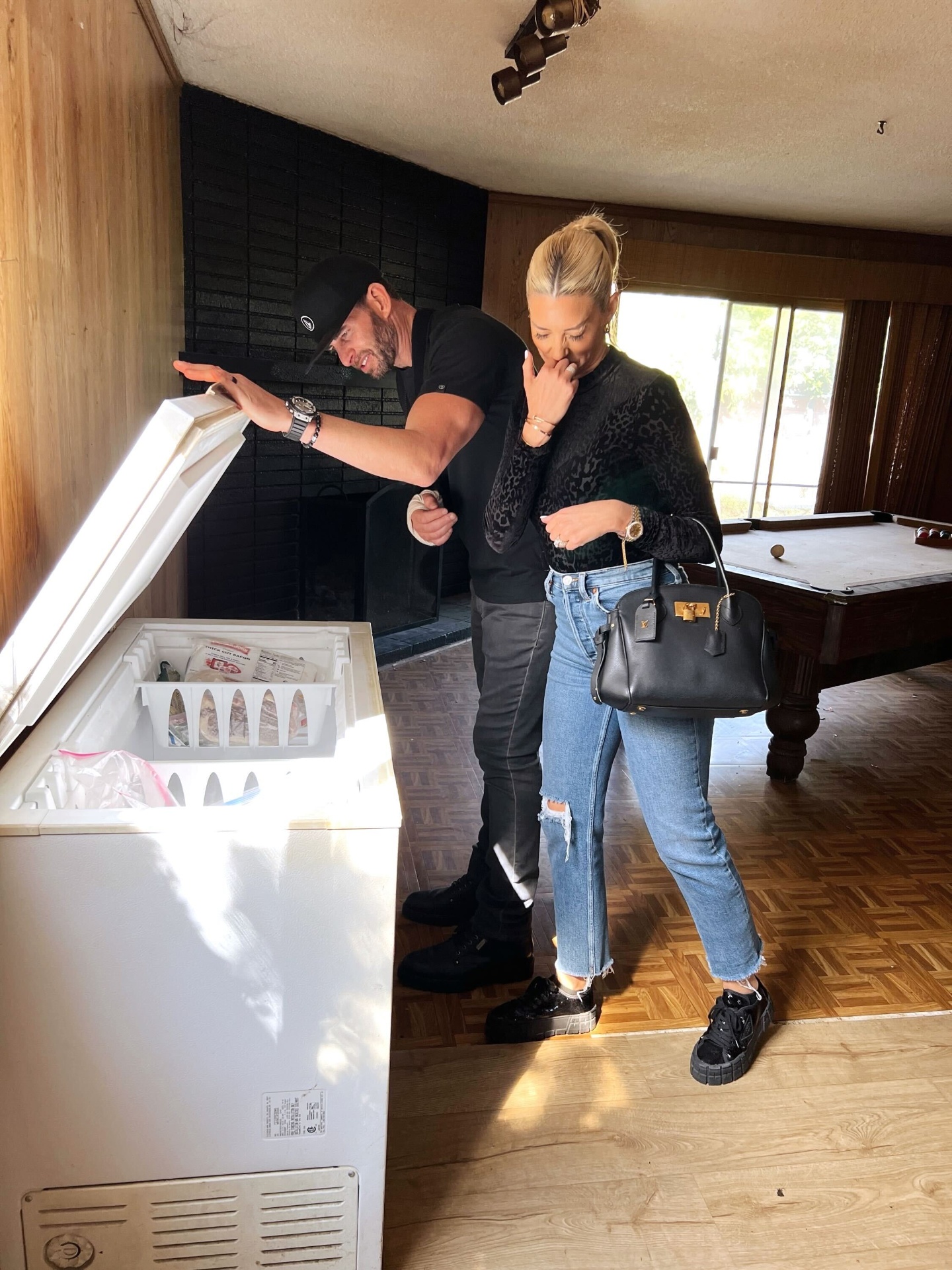 Couple inspecting a freezer in a wood-paneled room during a renovation walkthrough